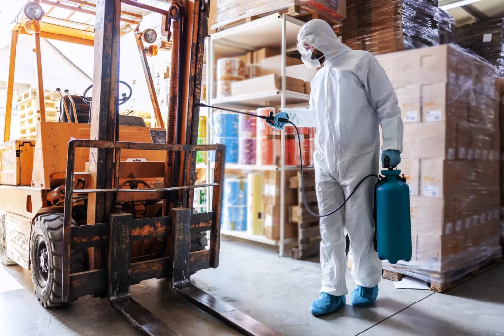 A worker using a professional pressure washer to clean a warehouse floor.