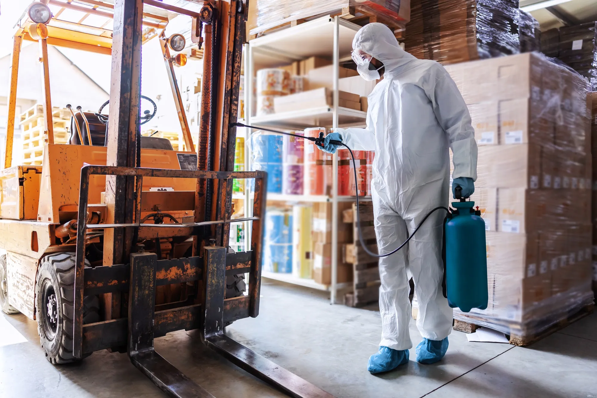 A worker using a professional pressure washer to clean a warehouse floor.